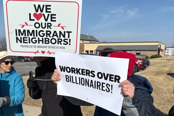 Photo of people holding signs that read "We Love Our Immigrant Neighbors" and "Workers Over Billionaires"