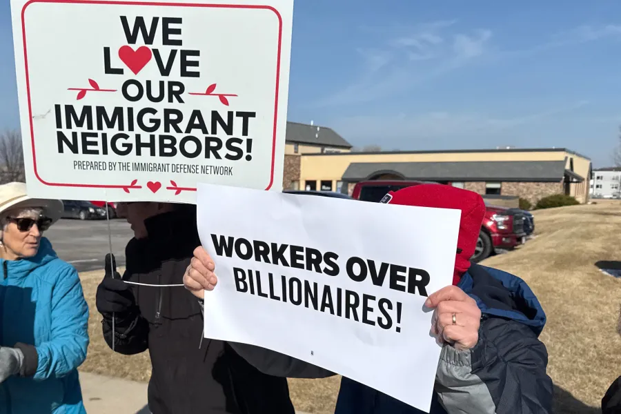 Photo of people holding signs that read "We Love Our Immigrant Neighbors" and "Workers Over Billionaires"